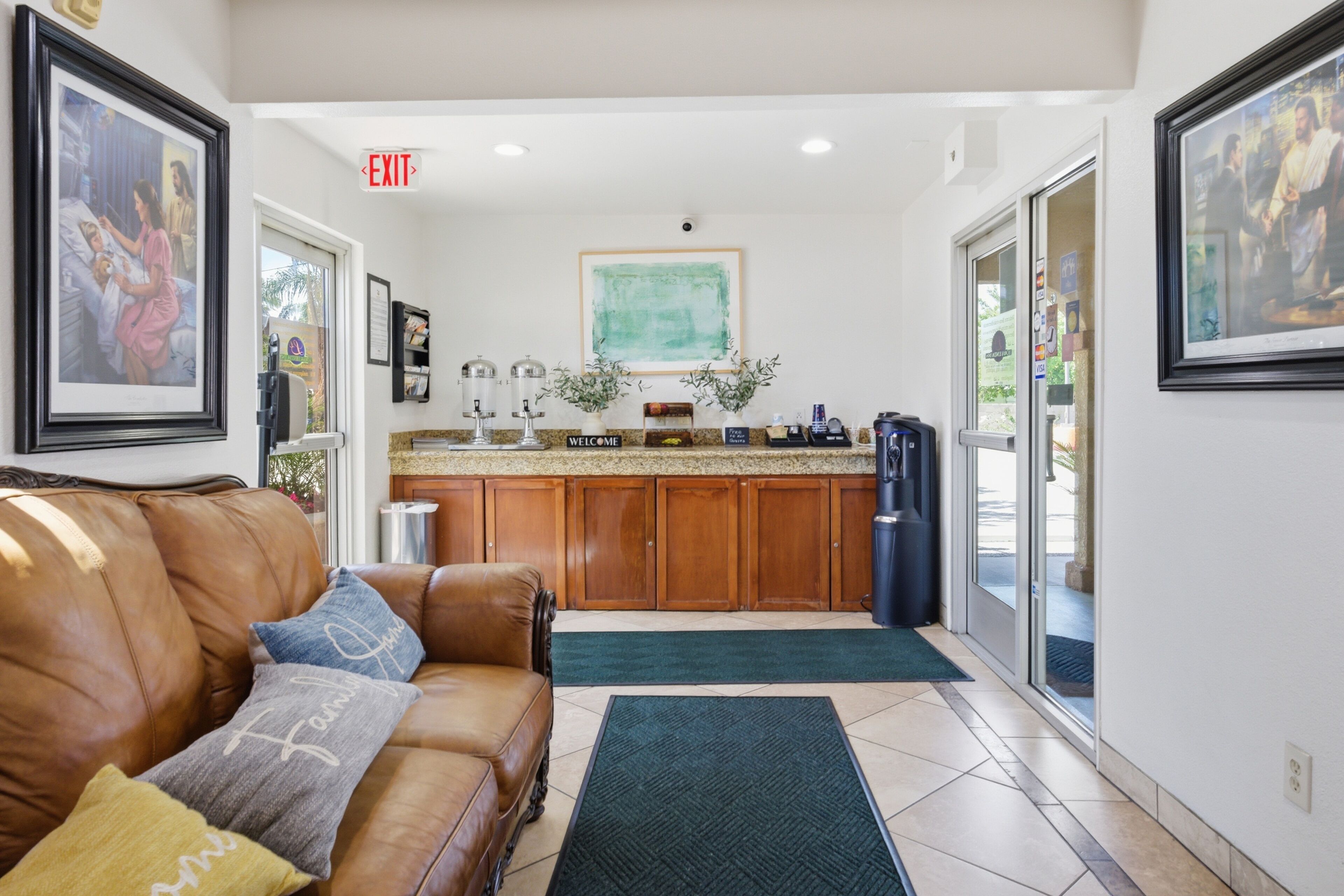 A spacious living area with a leather sofa, a kitchen with wooden cabinets, and framed artwork on the walls. - Loma Linda Inn (Loma Linda)