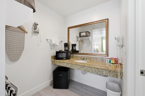A bathroom with a granite countertop, a sink, a mirror, a hairdryer, and a trash bin. - Loma Linda Inn (Loma Linda)
