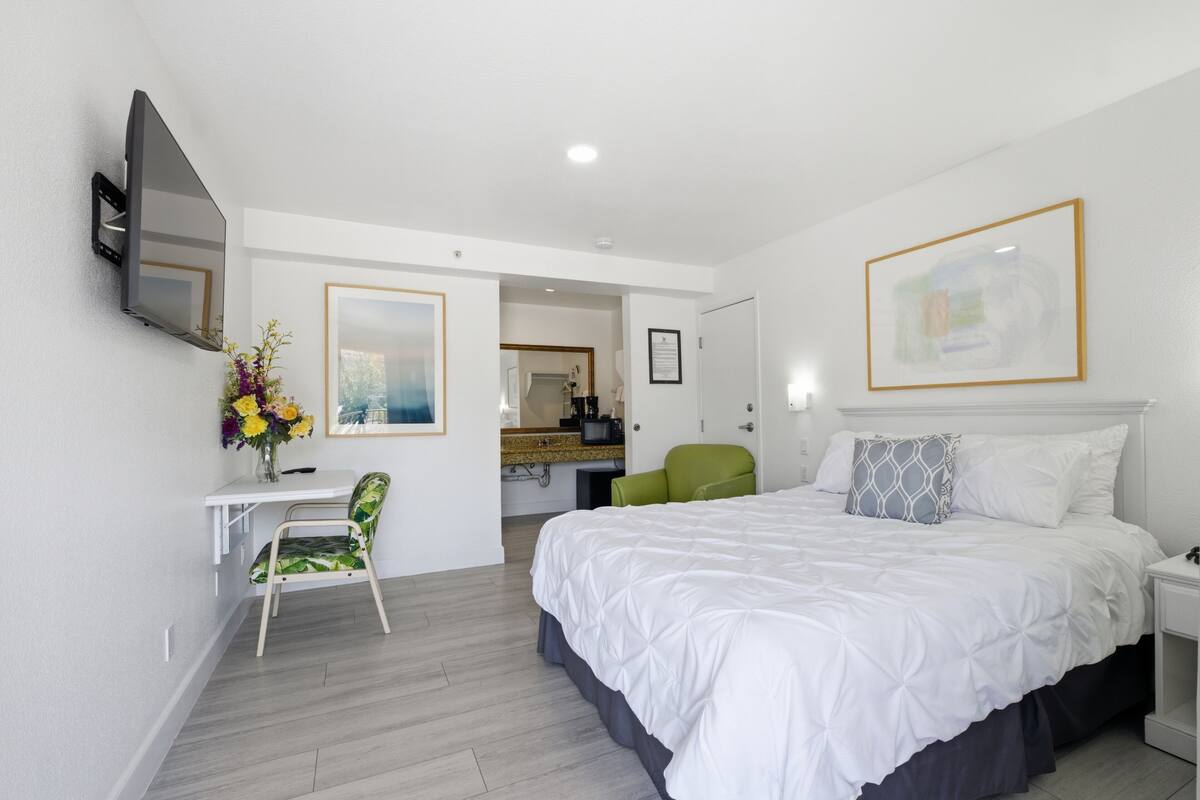 A hotel room with a bed, a desk, a chair, a TV, and a bathroom visible through an open door.