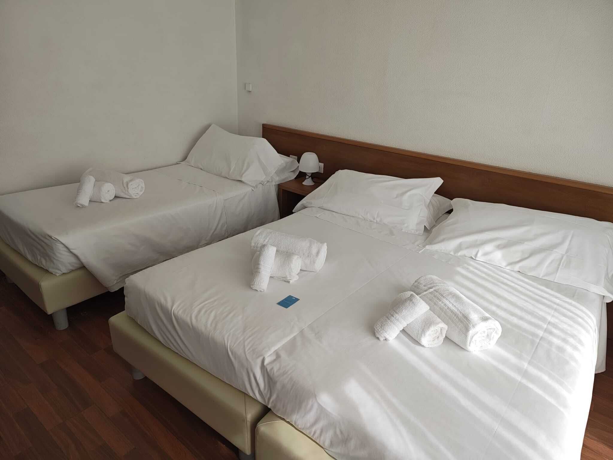Habitación de hotel con dos camas, cada una con ropa de cama blanca y toallas enrolladas.