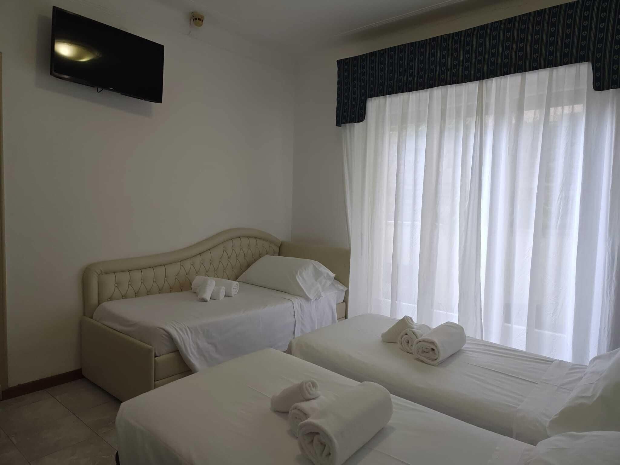 Habitación de hotel con dos camas, un televisor de pantalla plana y una ventana con cortinas traslúcidas.