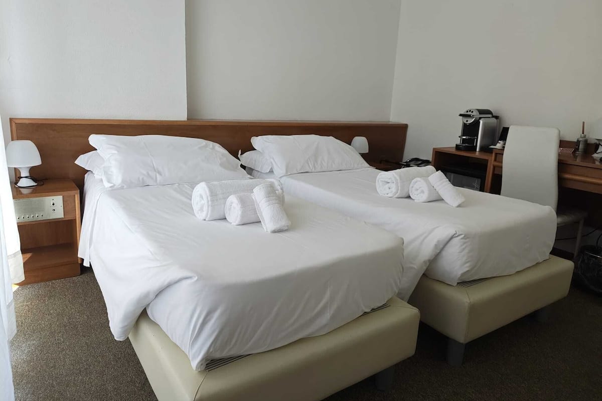 A hotel room with two beds, a desk, a chair, a lamp, and a coffee machine.