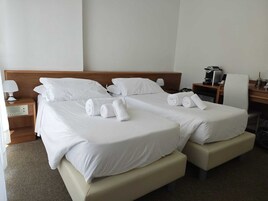 Una habitación de hotel con dos camas, un escritorio, una silla, una lámpara y una cafetera.