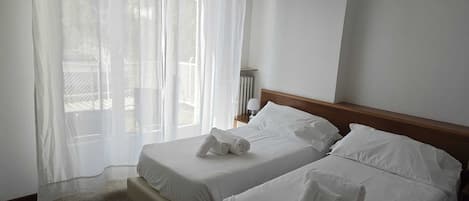 Habitación de hotel con dos camas, una ventana con cortinas translúcidas, aire acondicionado montado en la pared y una mesita con lámpara.