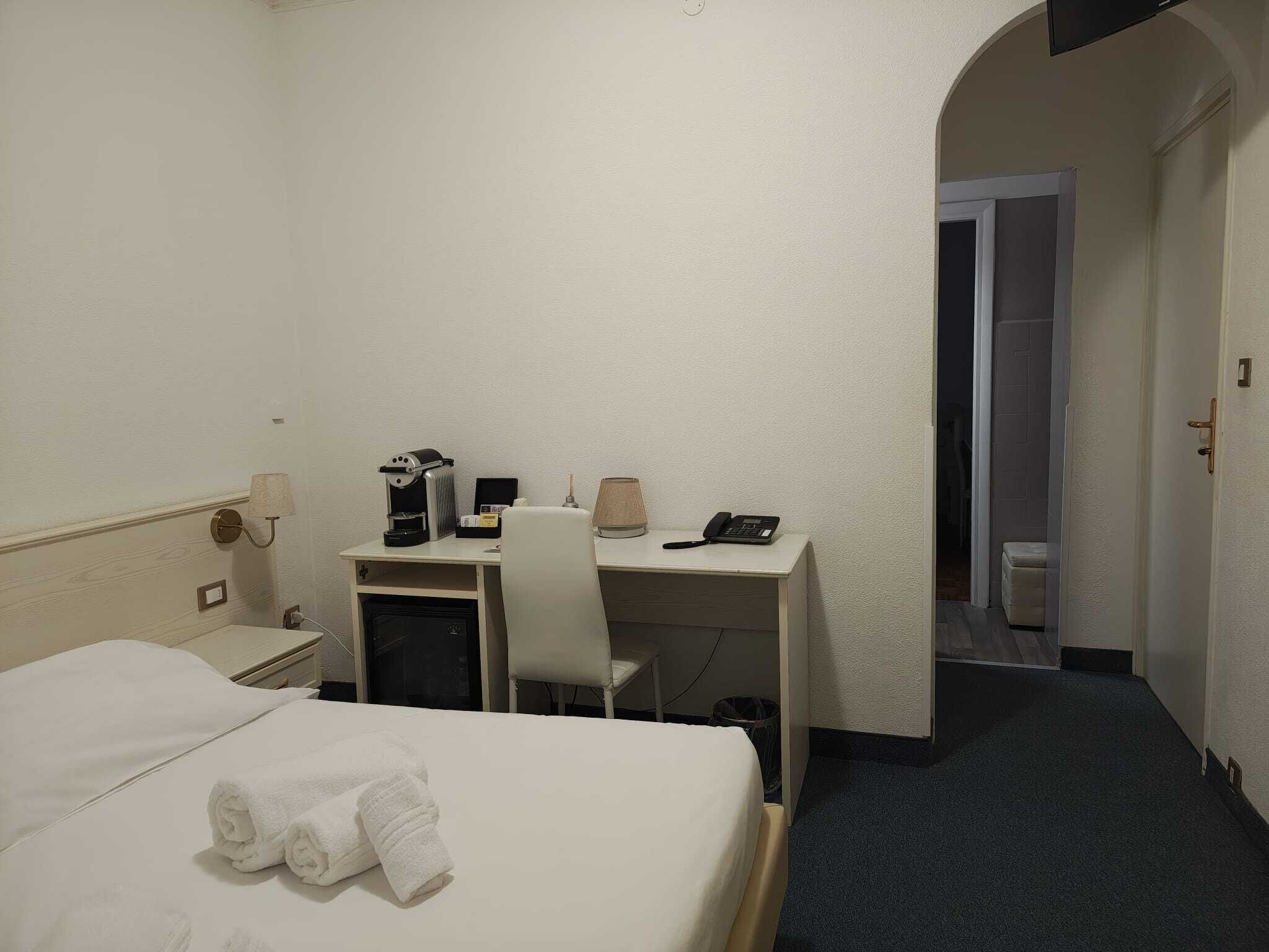A hotel room with a bed, a desk with a computer, a telephone, and a coffee maker.