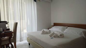 Una habitación de hotel con una cama, un escritorio con una silla, un radiador y una ventana con cortinas.