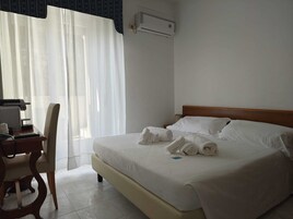 Una habitación de hotel con una cama, un escritorio con una silla, un radiador y una ventana con cortinas.