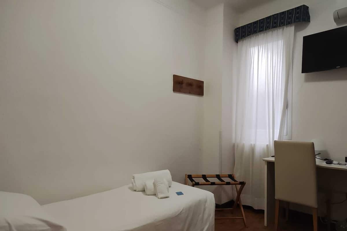 A hotel room with a bed, a desk, a chair, a TV, and a window with curtains.