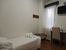 Quarto de hotel com cama, escrivaninha, cadeira, televisão e janela com cortinas.