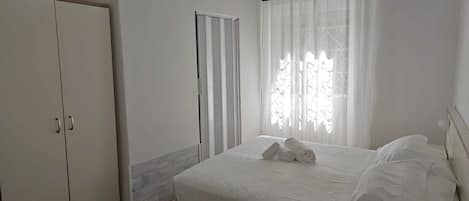 Un dormitorio con cama, armario, ventana con cortinas y radiador.