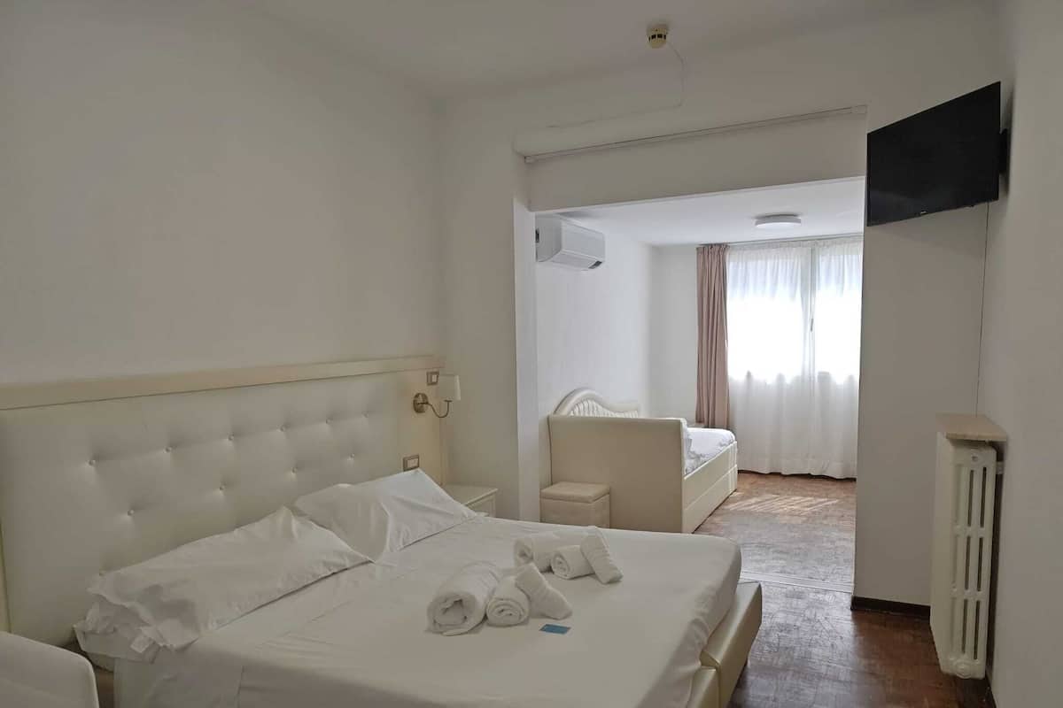 A hotel room with two beds, a TV mounted on the wall, and a radiator.