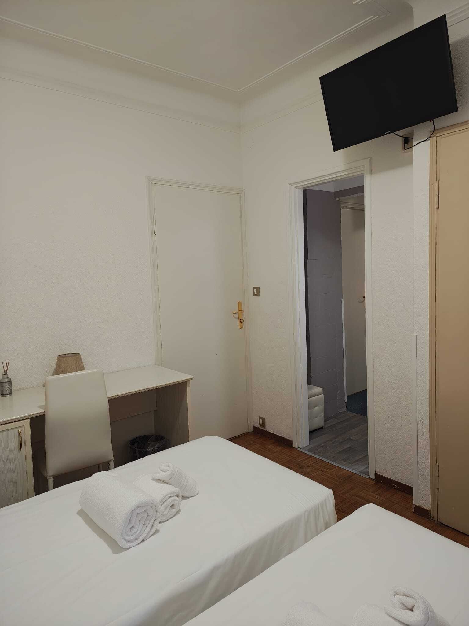 A hotel room with two beds, a desk, a chair, a TV, and a bathroom visible through an open door.