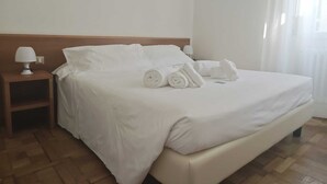 A hotel room with a bed, pillows, a nightstand with a lamp, and a wooden floor. - Hotel Rio (Sanremo)
