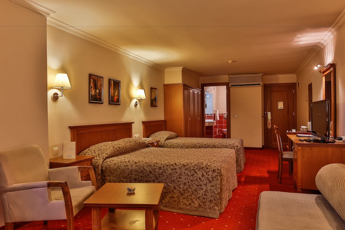 A hotel room with two beds, a desk, a chair, a small table, and a television.