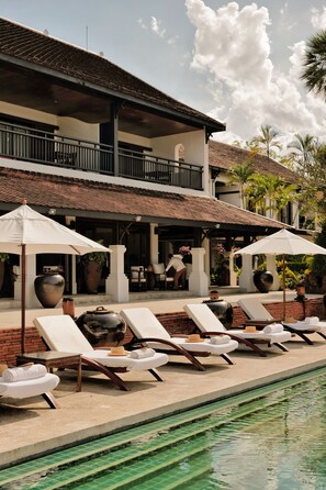 A poolside area with lounge chairs and umbrellas, a building with a tiled roof, and a clear sky. - La Résidence Phou Vao (Luang Prabang)