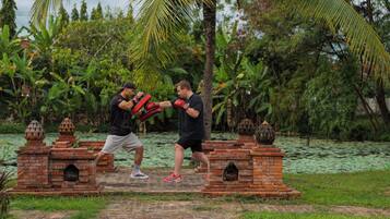 Dos personas practicando artes marciales sobre una plataforma de ladrillo, rodeadas de abundante vegetación y un cuerpo de agua.