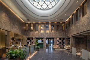 Un'ampia hall con soffitto alto, una reception, un'area salotto e vista attraverso una grande finestra.