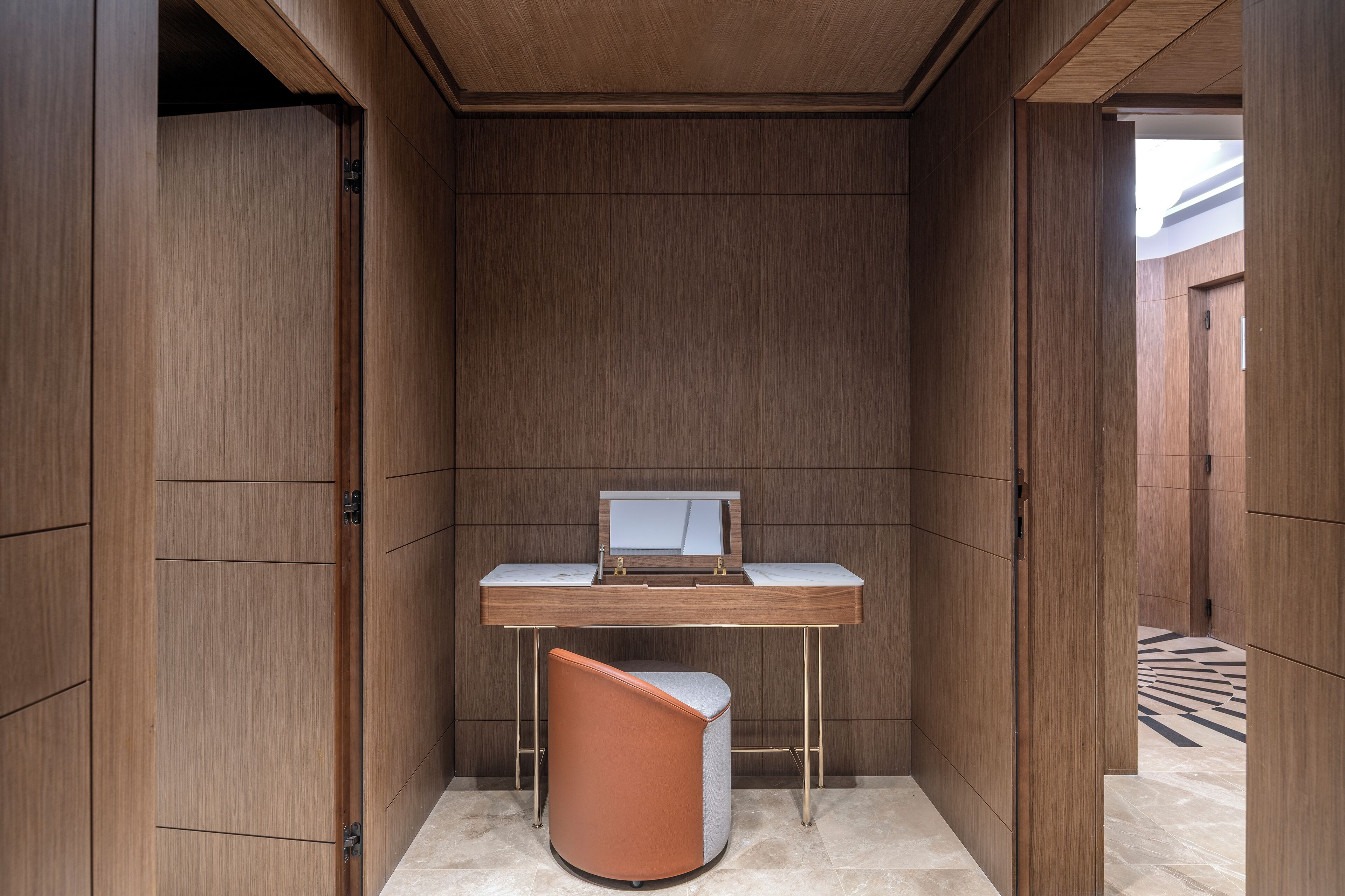 A compact, modern room with a wooden panel wall, a white desk with a computer, and a unique orange chair.