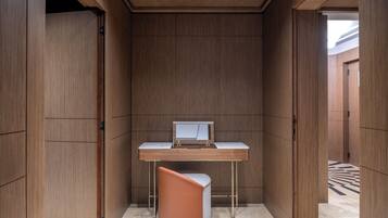A compact, modern room with a wooden panel wall, a white desk with a computer, and a unique orange chair.