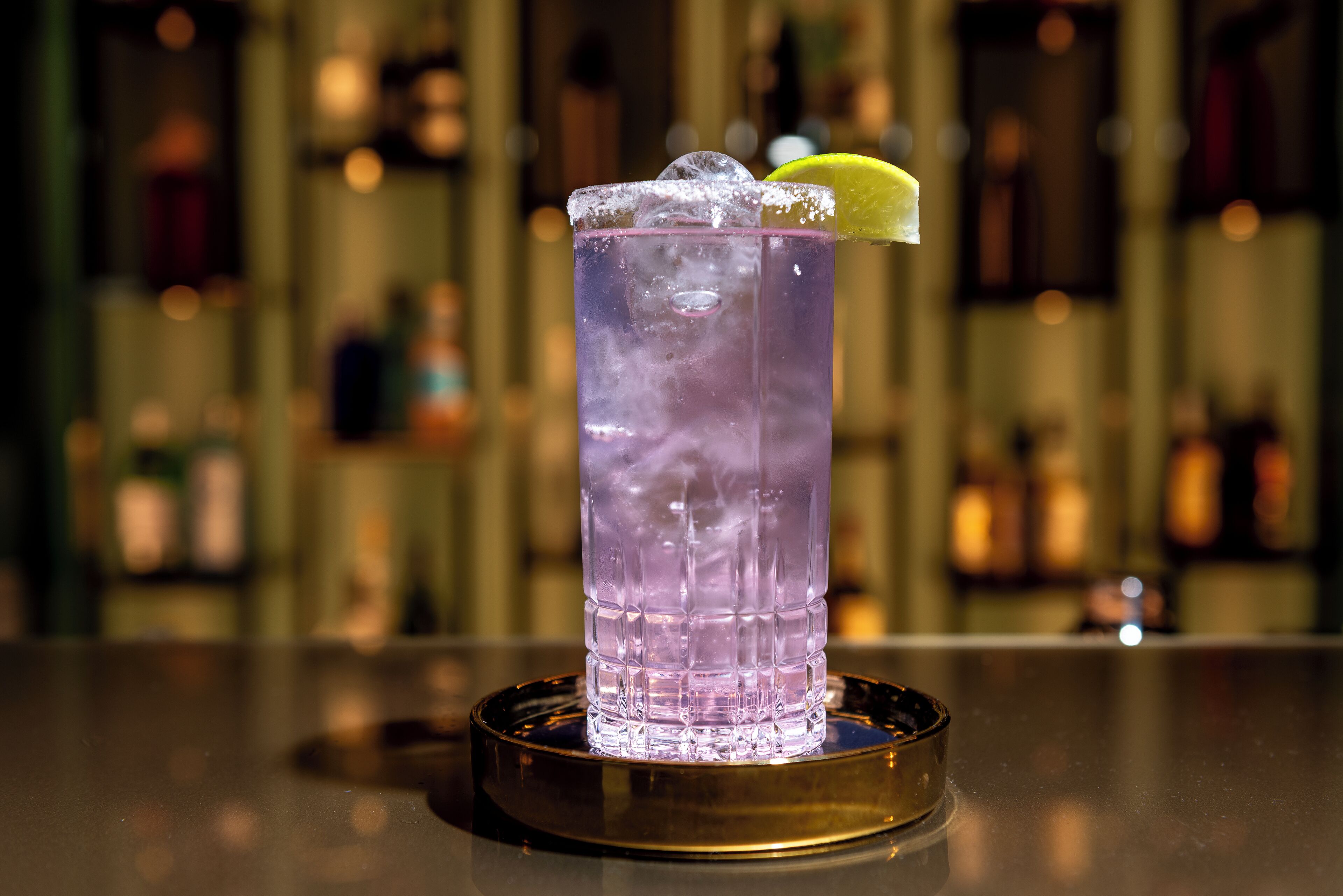 A bar setting with a tall glass of purple drink, ice, and a lime wedge.