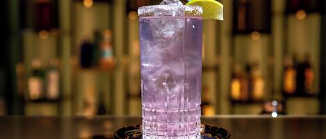Un bar con un vaso alto de bebida morada, hielo y una cuña de limón.