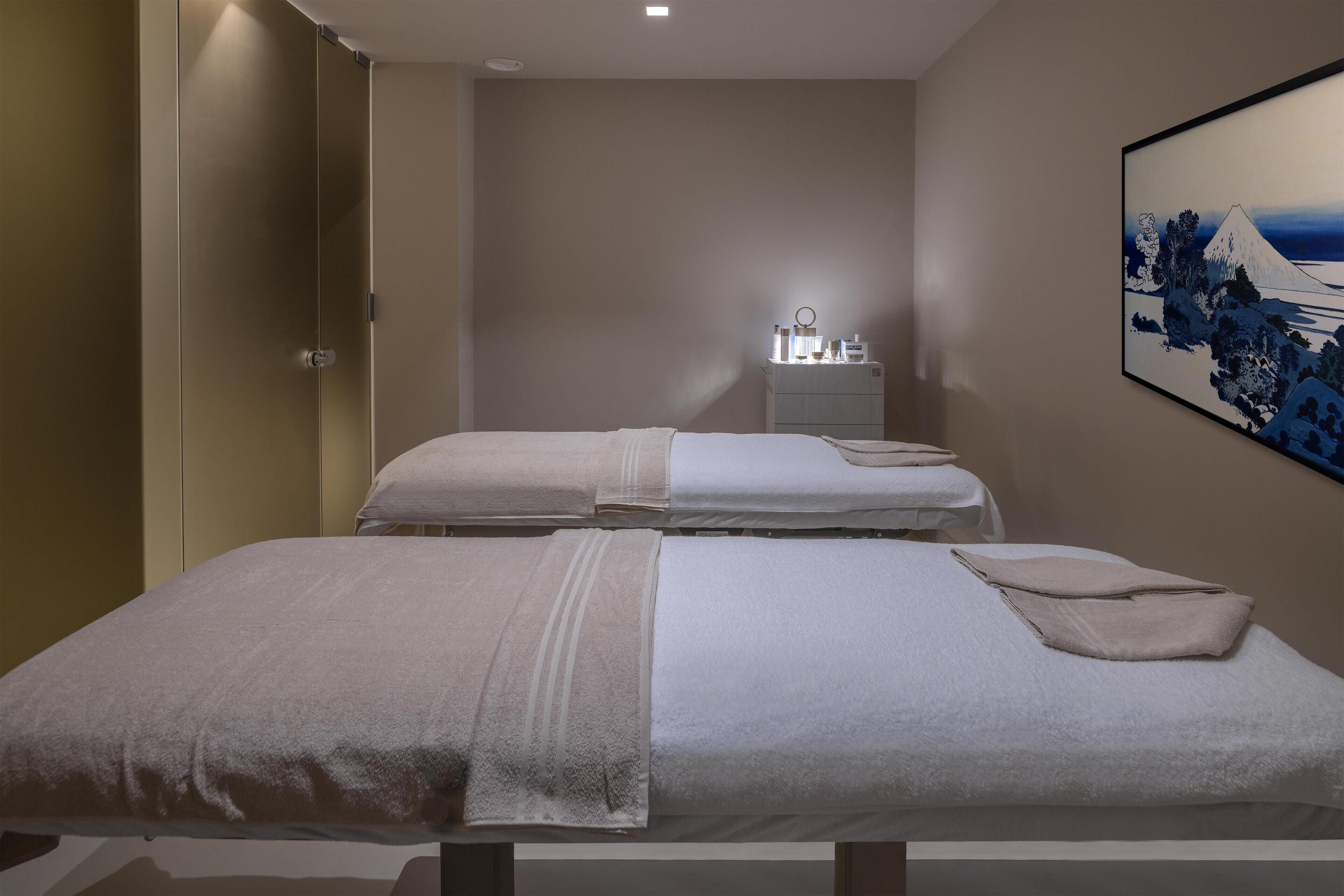 A room with two beds, a small bedside table with toiletries, and a wall-mounted painting.