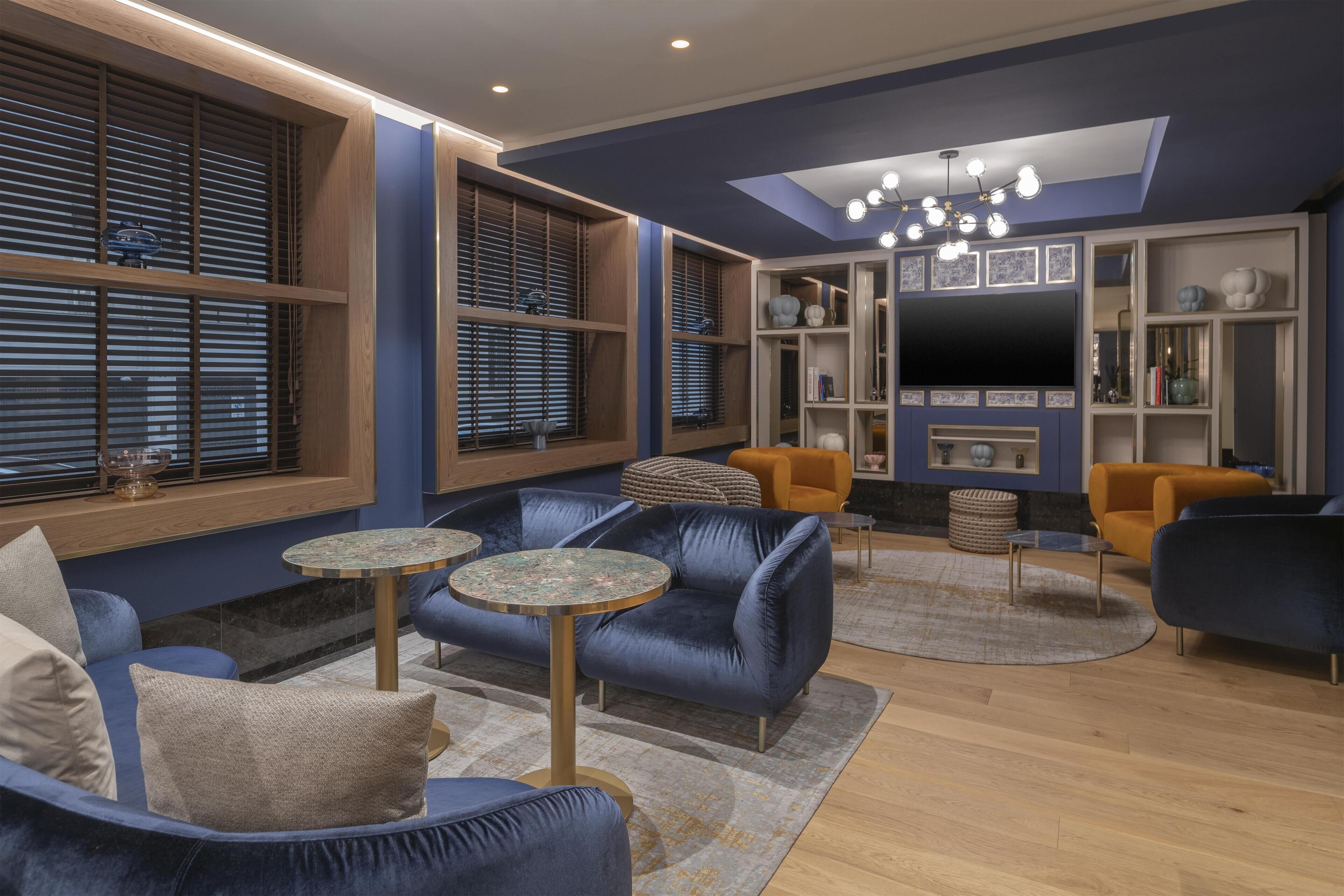 A modern living room with blue sofas, round tables, and a flat-screen TV.