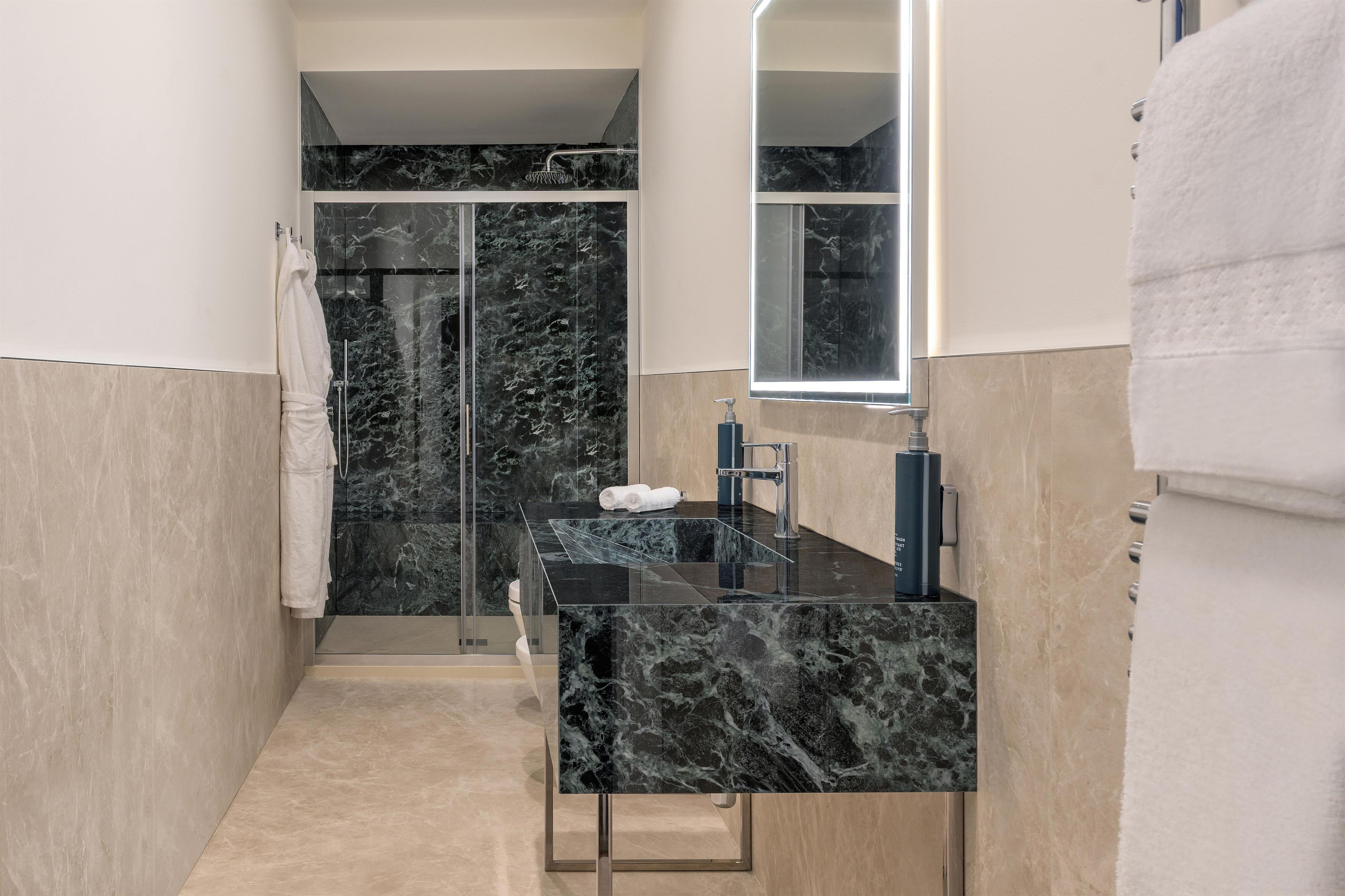 A modern bathroom with a glass shower enclosure, a black marble sink, and a mirror above the sink.