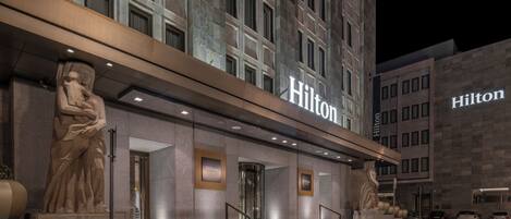 A Hilton hotel entrance with a grand staircase, large stone statues, and a modern facade.