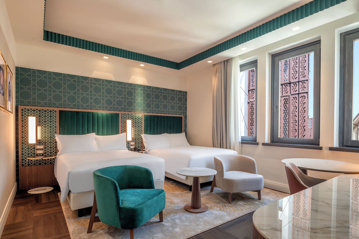 A hotel room with a large bed, two smaller beds, a green armchair, a round coffee table, and a dining table.