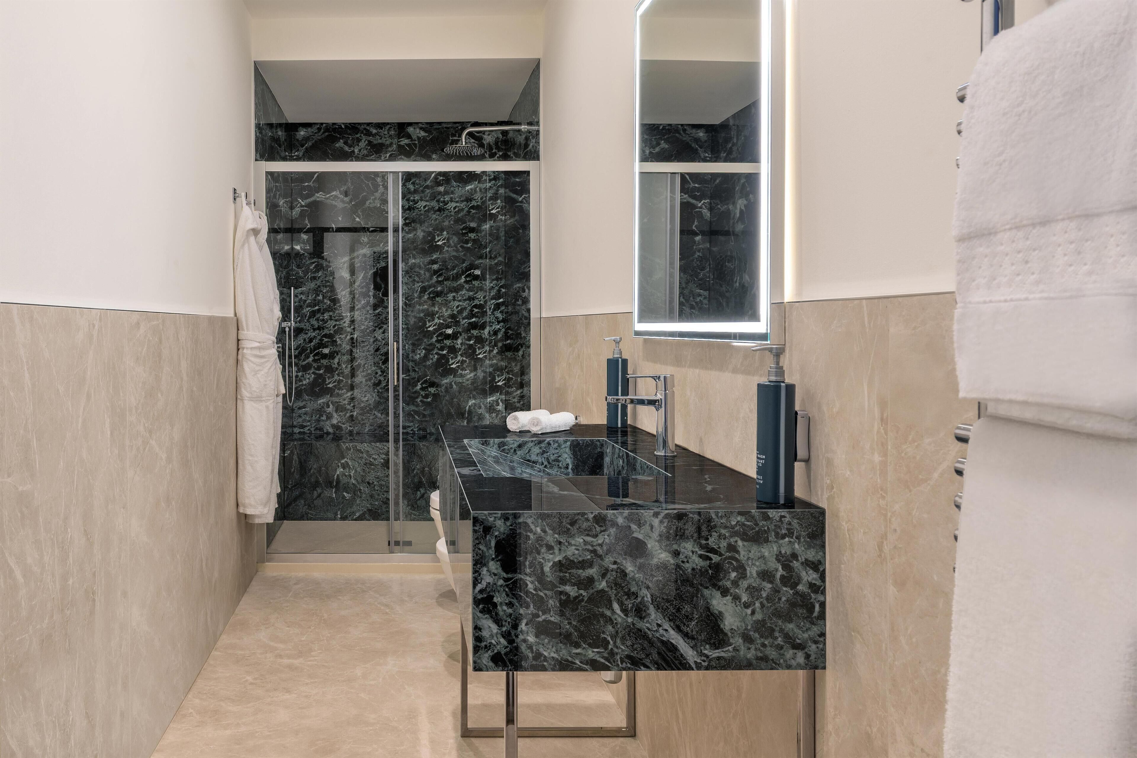 A modern bathroom with a black marble vanity, a glass shower enclosure, and a large mirror.