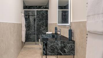 A modern bathroom with a black marble vanity, a glass shower enclosure, and a large mirror.