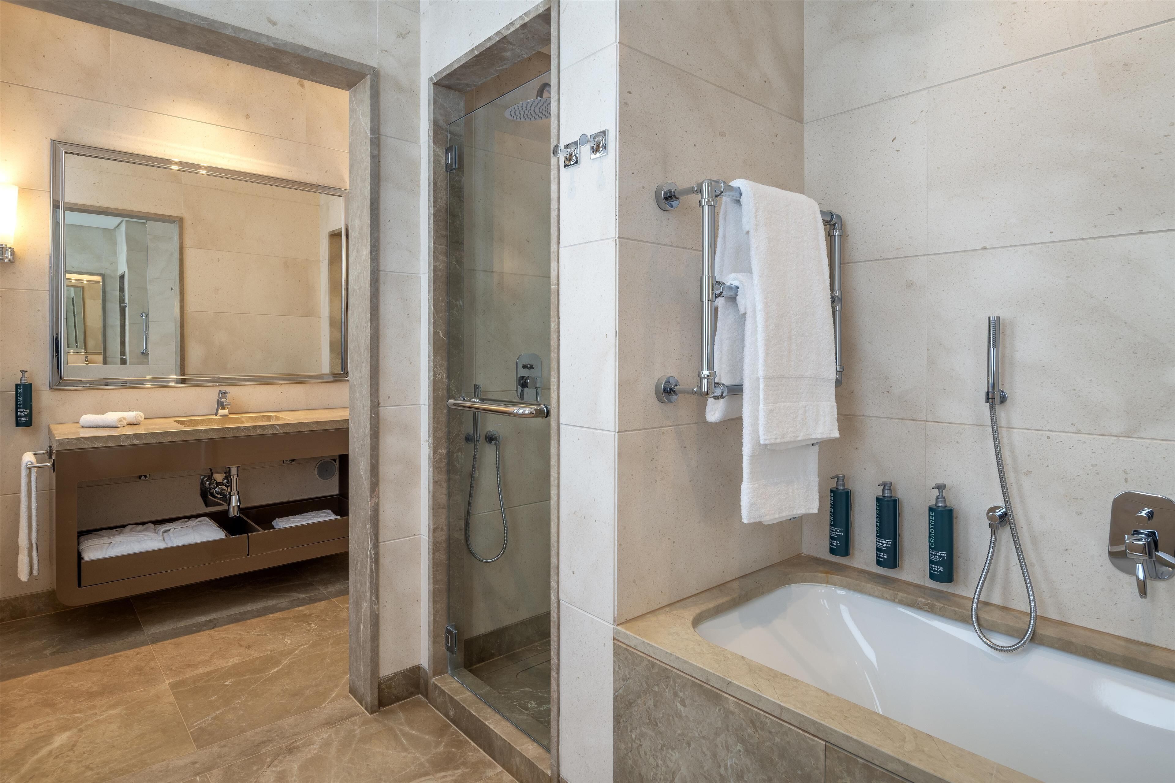Une salle de bain moderne dotée d’une douche à parois de verre, d’un grand miroir, d’une baignoire et d’un meuble-lavabo avec un porte-serviettes.