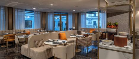 A modern hotel lobby with a seating area featuring sofas and chairs, a buffet table with food, and large windows offering views of the city.