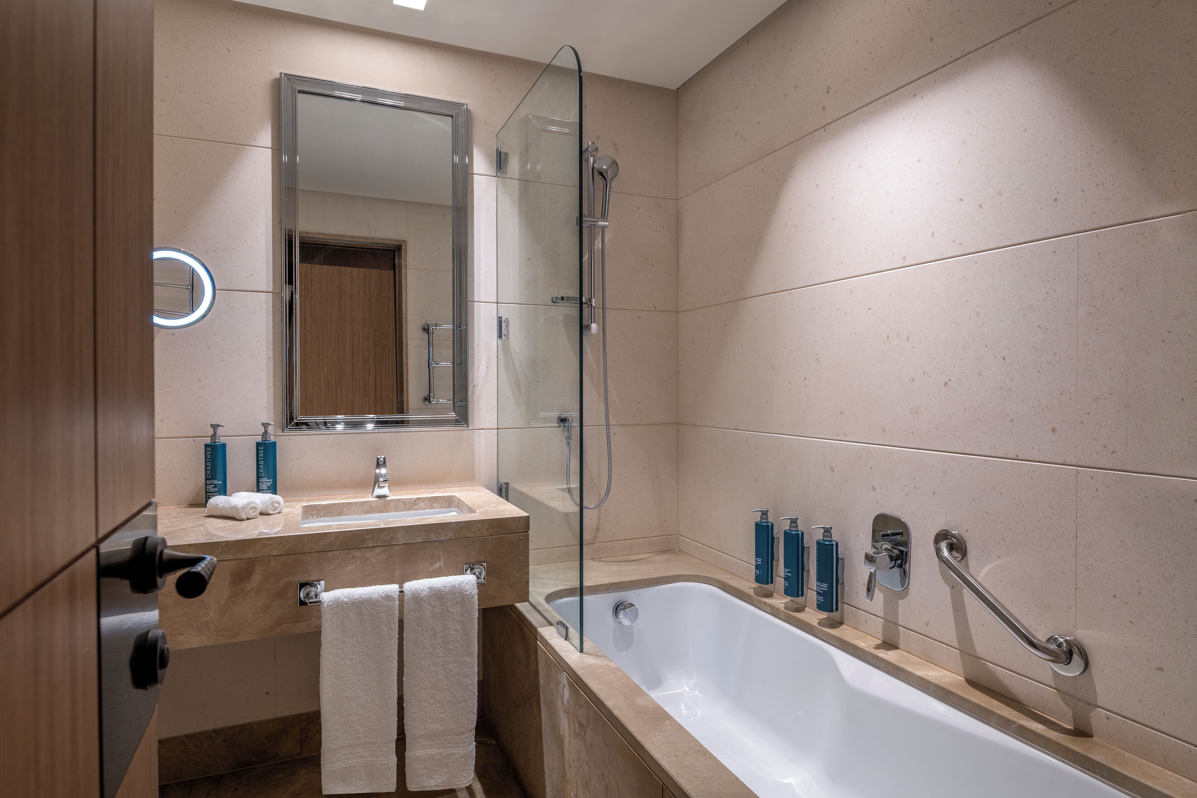 Ein modernes Badezimmer mit Badewanne, Duschkabine aus Glas, Waschtisch mit Spiegel und Pflegeprodukten.