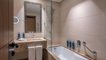 Ein modernes Badezimmer mit Badewanne, Duschkabine aus Glas, Waschtisch mit Spiegel und Pflegeprodukten.