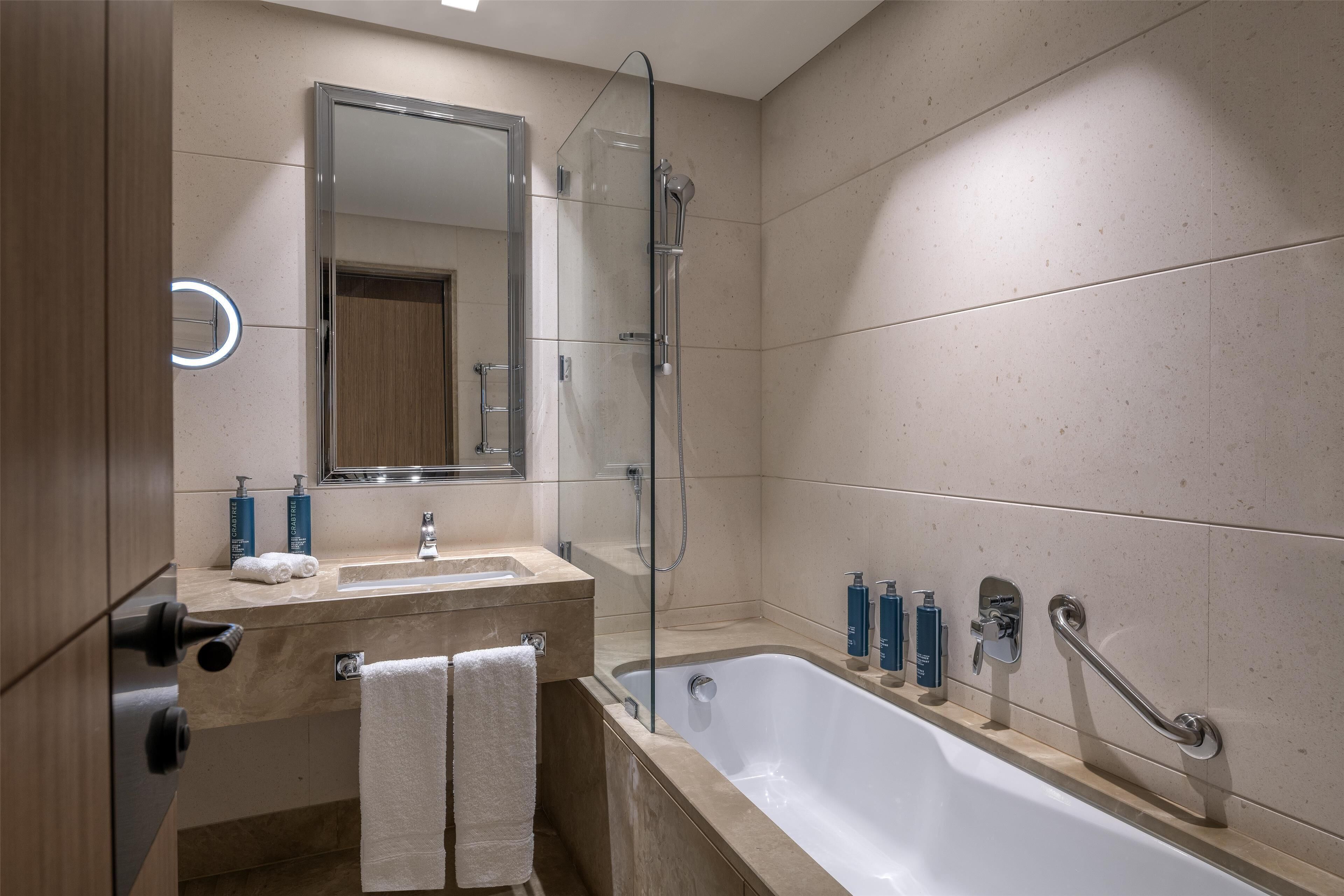 Et moderne badeværelse med badekar, bruseniche med glasvægge, vaskebord med spejl og toiletartikler på bordet.
