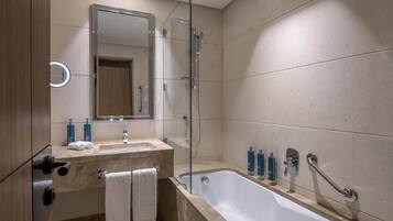 Et moderne badeværelse med badekar, bruseniche med glasvægge, vaskebord med spejl og toiletartikler på bordet.
