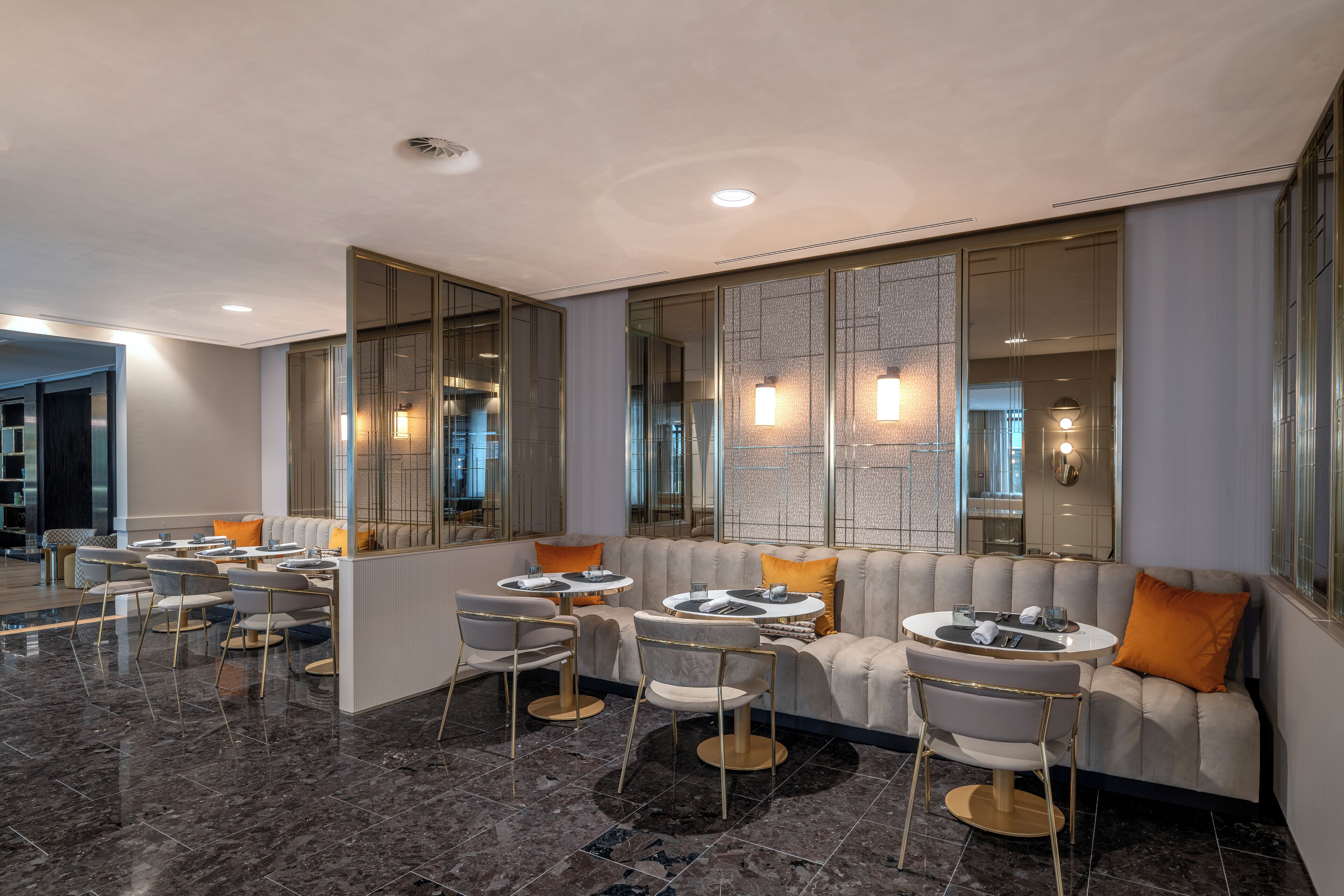A modern hotel lobby with a seating area, marble flooring, and large mirrors.