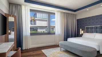 A modern hotel room with a large bed, a desk, and a view of the cityscape.
