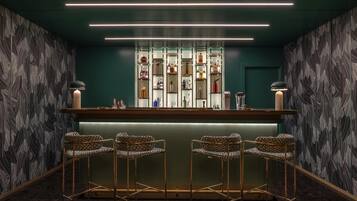 A bar area with a modern design, featuring a bar counter, four patterned bar stools, and a variety of bottles on shelves.