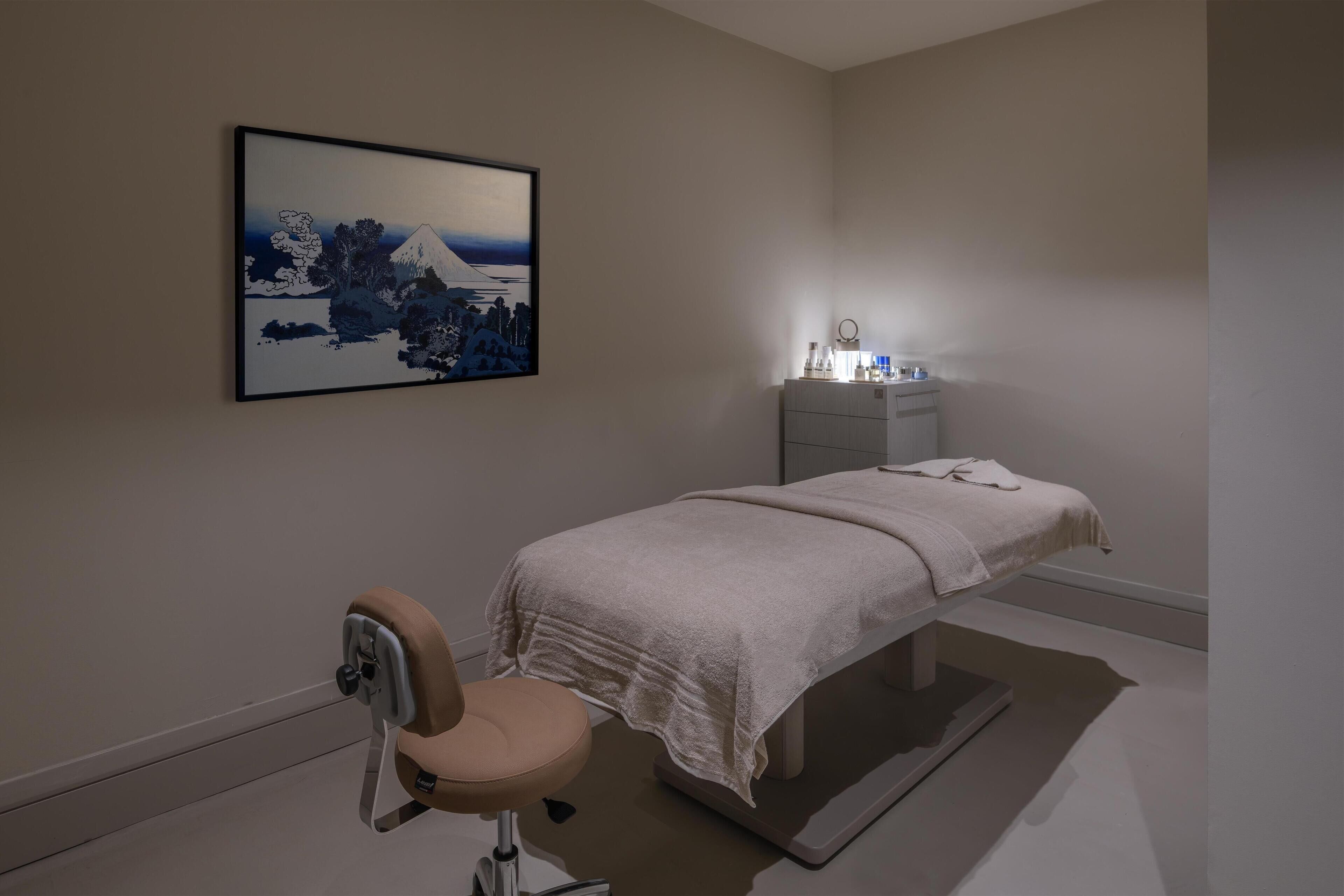 A modern bedroom with a bed, a chair, a bedside table with a lamp, and a framed artwork on the wall.