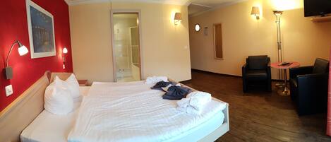 A hotel room with a bed, two bedside lamps, a TV, a chair, and a small table.