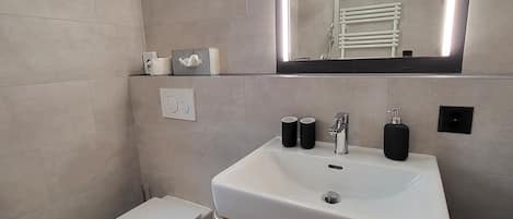 Un baño moderno con un lavamanos blanco, un espejo y un inodoro.