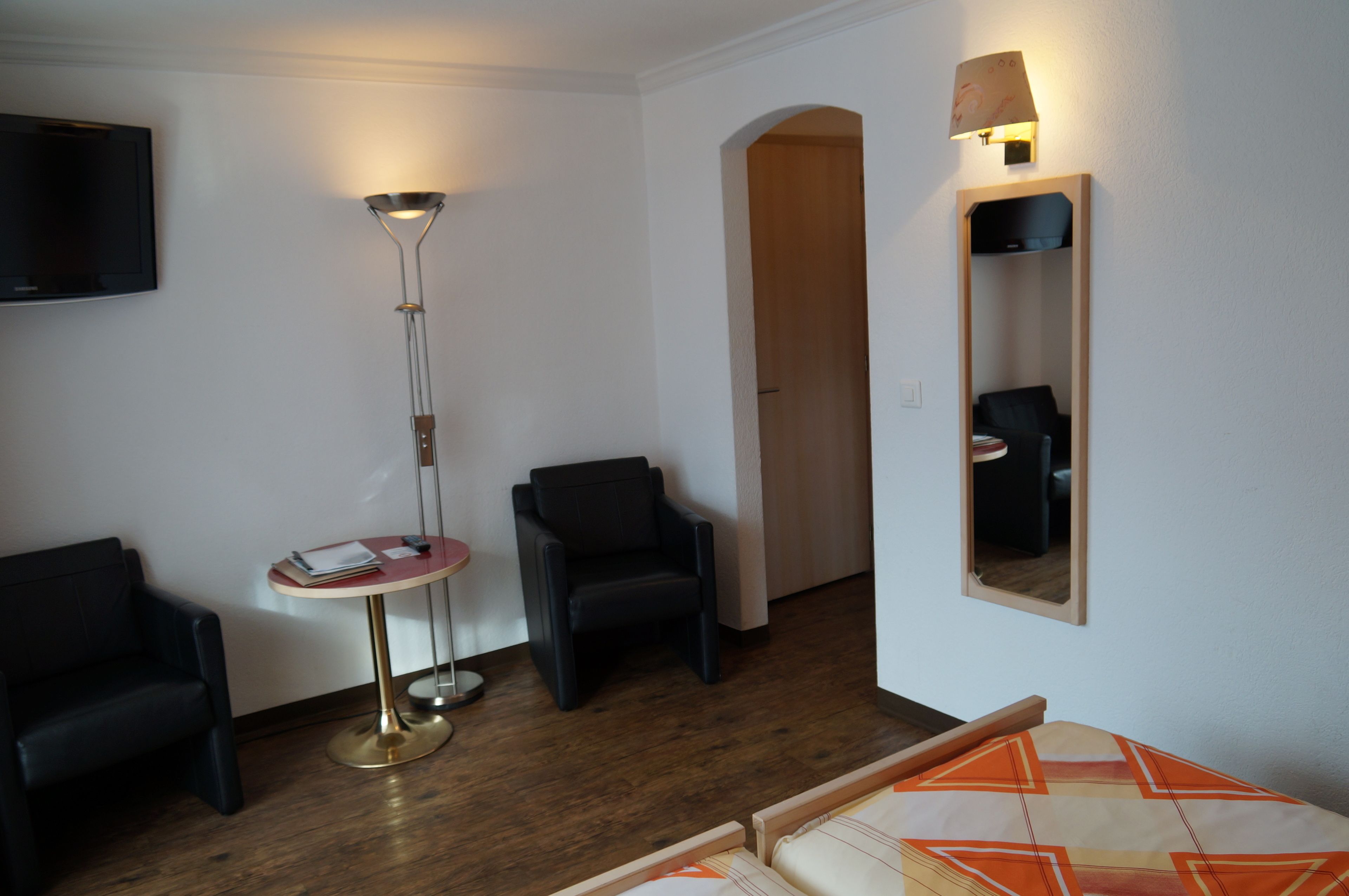 Una habitación con televisión, una lámpara de pie, dos sillones, una mesita redonda y un espejo en la pared.