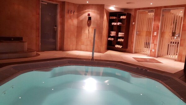 A spa area with a hot tub, tiled walls, and shelves with towels.