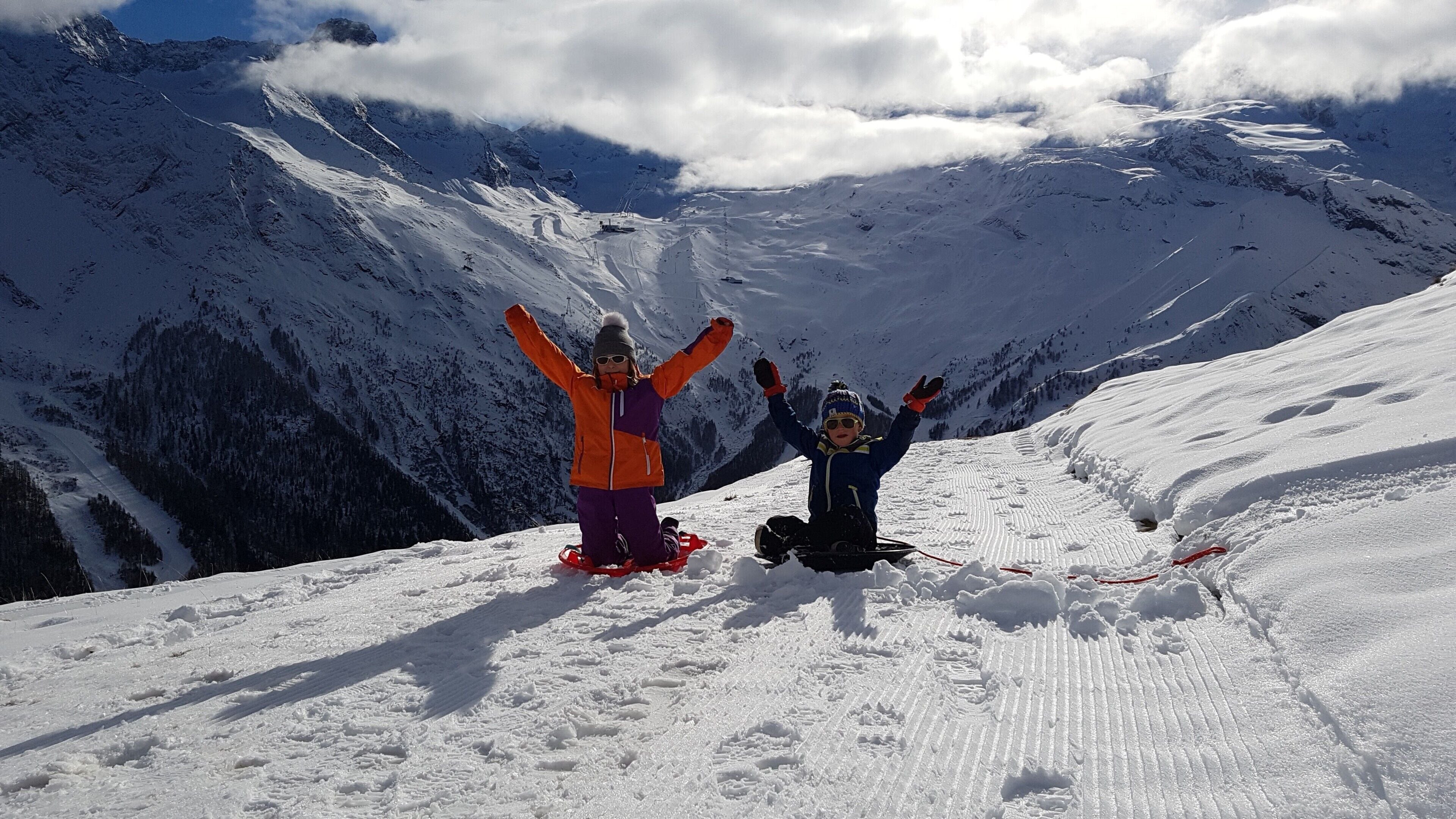 Two people on a snowy mountain with a clear sky and mountains in the background.