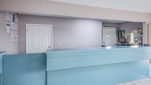 Ein Empfangsbereich mit einem hellblauen Empfangstresen, einer weißen Tür und einer Pinwand mit Dokumenten.