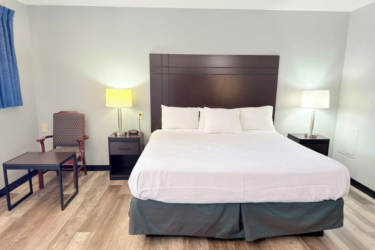 Habitación de hotel con una cama grande, dos mesitas de noche con lámparas, un escritorio pequeño y una silla.