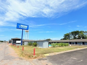A hotel with a large blue sign, a water tower, and a parking lot. - Americas Best Value Inn Giddings (Giddings)